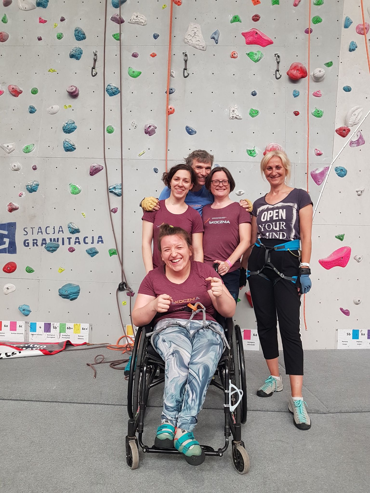 Zdjęcie przedstawia obraz osób z niepełnosprawnościami o różnych schorzeniach na ściance wspinaczkowej. Parawspinaczka. Paraclimbing. Niepełnosprawność. Sport OzN.