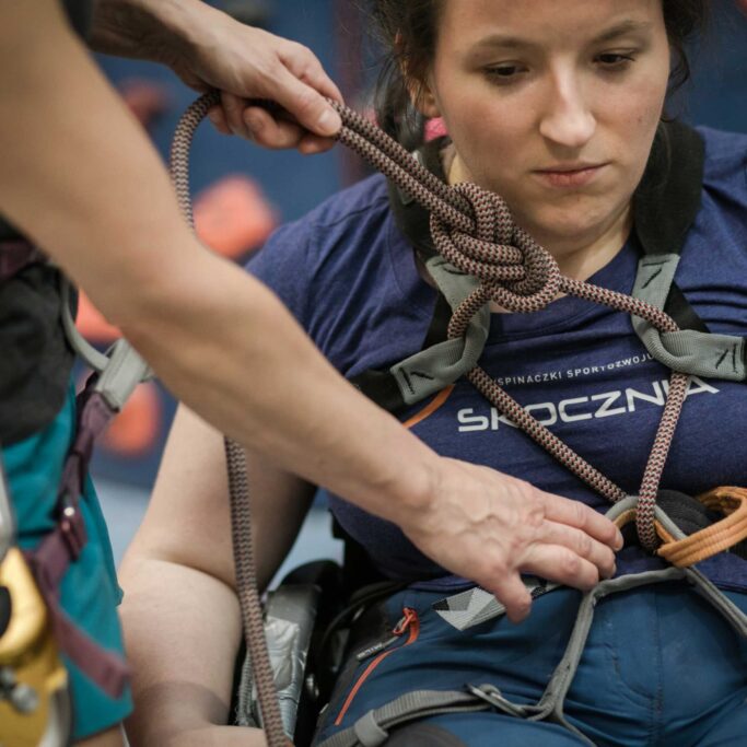 Parawspinaczka. Na zdjęciu instruktor sprawdza, czy osoba z niepełnosprawnością ma prawidłowo założoną uprząż. Sport OzN. Paraclimbing
